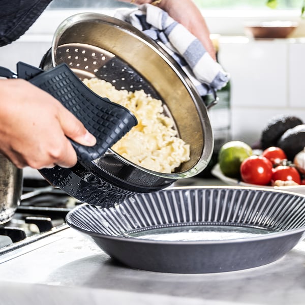 Asmuo pila maistą iš juodo KLOCKREN kiaurasamčio į keptuvę. Virtuvės prekystalis su produkcija.