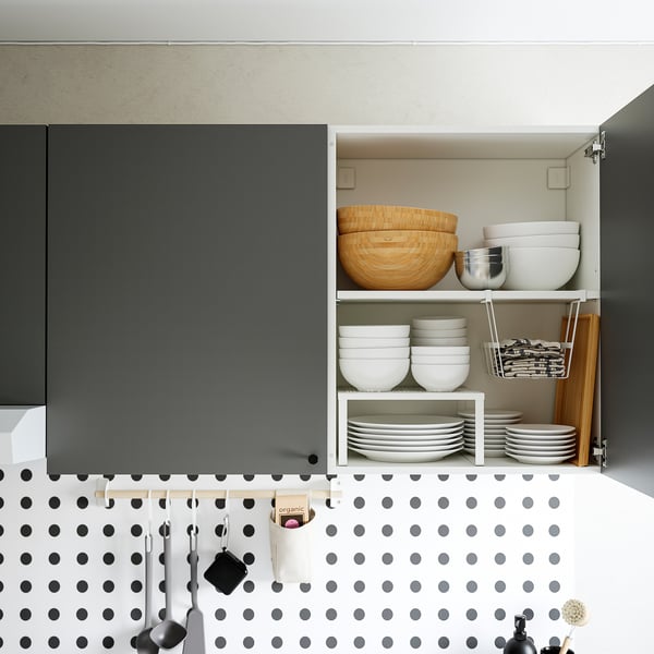 Atidarykite virtuvės spintelę su lėkštėmis ir dubenėliais, žemiau polka dot backsplash ir kabančius indus.