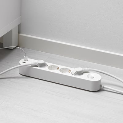 Baltas daugiafunkcis lizdas su USB prievadais ant medinių grindų. Prijungti du kabeliai, vienas su balta jungtimi.