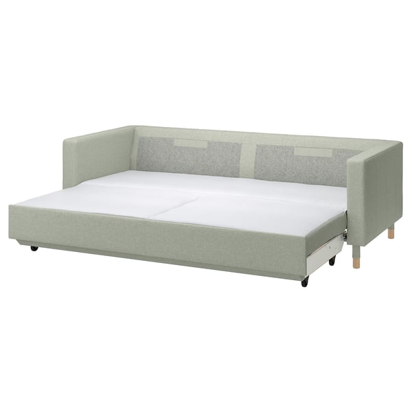 Moderni šviesiai žalia sofa-lova su medinėmis kojomis ir pliušinėmis pagalvėlėmis.