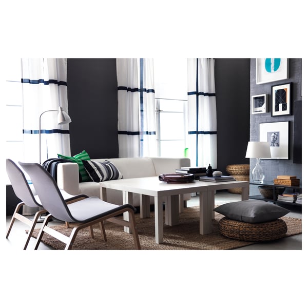 Moderni svetainė su baltu LERSTA grindų šviestuvu, balta sofa, pilkomis pagalvėlėmis, medinėmis kėdėmis, stačiakampiu stalu, kilimu ir sienų menu.