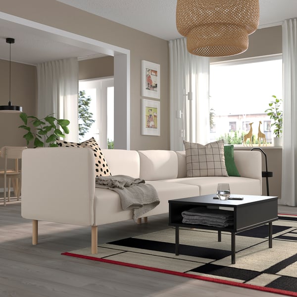 Moderni svetainė su LILLEHEM sofa, juodu kavos staliuku, kilimu, augalais ir dideliu langu.