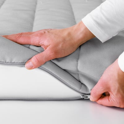 Asmuo, laikantis pilką porolono čiužinį su užtrauktuku. Jis skirtas lycksele sofa-lova, su nuimamu, plaunamu dangteliu, kad būtų lengva valyti.