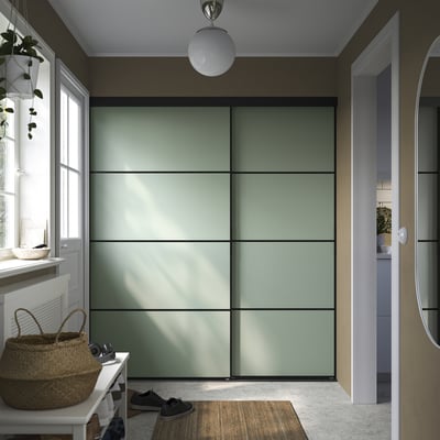 Modernus kambarys su didele žalia stumdoma spinta, balta pakabinama šviesa ir pintu krepšiu prie lango su natūralia šviesa.
