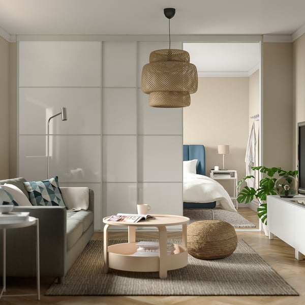 Moderni svetainė su pilka sofa, mėlynais akcentais, mediniu kavos staliuku, arbatinuku, žurnalu, austine taburete, stiklinėmis durimis, ryškiomis, neutraliomis spalvomis.