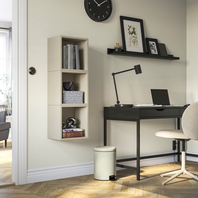 Modernus namų biuras su minimalistiniu rašomuoju stalu, kėde, lempa, šiukšliadėže ir knygomis.