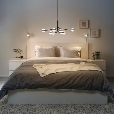 Modernus miegamasis su STORSLINGA šviestuvu virš lovos, minkštas apšvietimas, neutralūs skalbiniai, augalai, minimalistinis menas, jauki atmosfera.