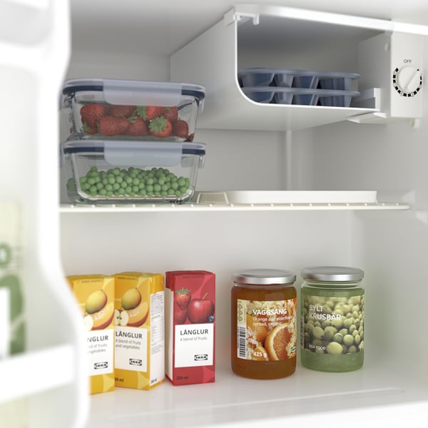 Nedidelis šaldytuvas su vaisių sultimis, uogiene ir konservuotais žirneliais viduje, įskaitant lentyną ir ledo dėklą.