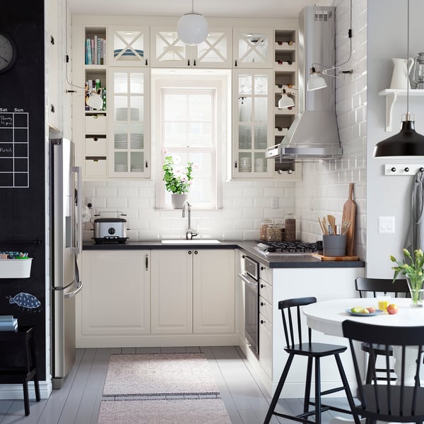 Современная кухня с белыми шкафами, черными стульями, бытовой техникой из нержавеющей стали и ковром.