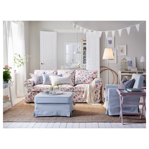 Светлая гостиная с цветочным диваном, голубыми акцентами, естественным освещением, подвесными украшениями и деревянным полом.