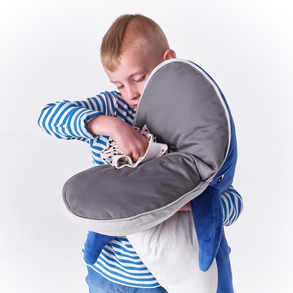 Ребенок обнимает голубого кита, плюшевую игрушку. Игрушка имеет серый круглый рот и сине-белые полосы.