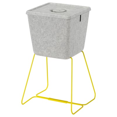 Серая фетровая корзина BRÄNNBOLL с желтой подставкой, крышкой и отверстием для кабеля для игровых аксессуаров.