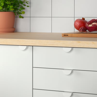Современная кухонная стойка с белыми ящиками с ручками DRAGSMARK, деревянной столешницей, гранатами и растением.