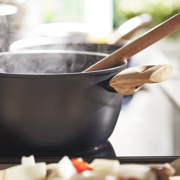 Черная кастрюля с деревянной ручкой, готовящаяся на пару на плите, с антипригарным керамическим покрытием.