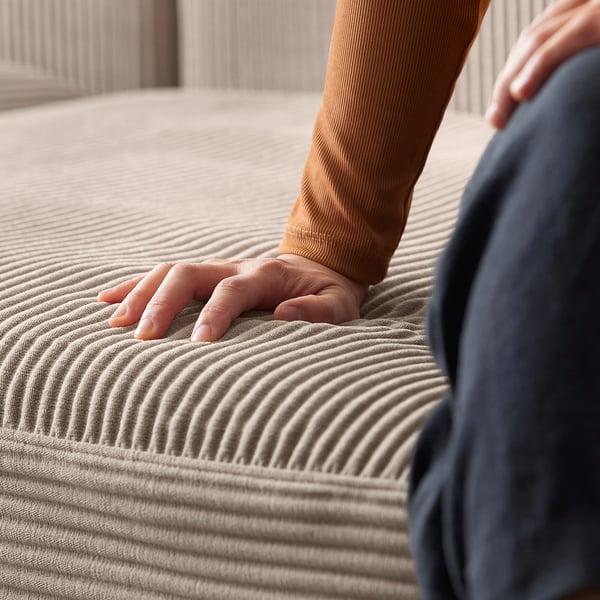 Человек прикасается к бежевому дивану JÄTTEBO с волнистой текстурой от ikea, демонстрируя его удобную ткань, похожую на вельвет.