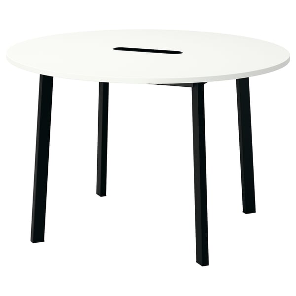 Изображен современный круглый белый стол для совещаний с четырьмя черными металлическими ножками, и слотом для прокладки кабелей.