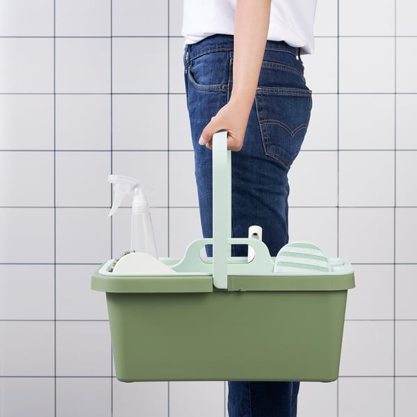 Человек, держащий зеленое ведро для чистки PEPPRIG с ручкой, содержащее пульверизатор и инструменты для очистки.
