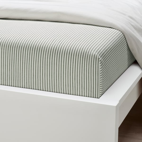 Аккуратно заправленная кровать с полосатым наматрасником, скорее всего из высококачественного хлопка, на белом каркасе кровати.