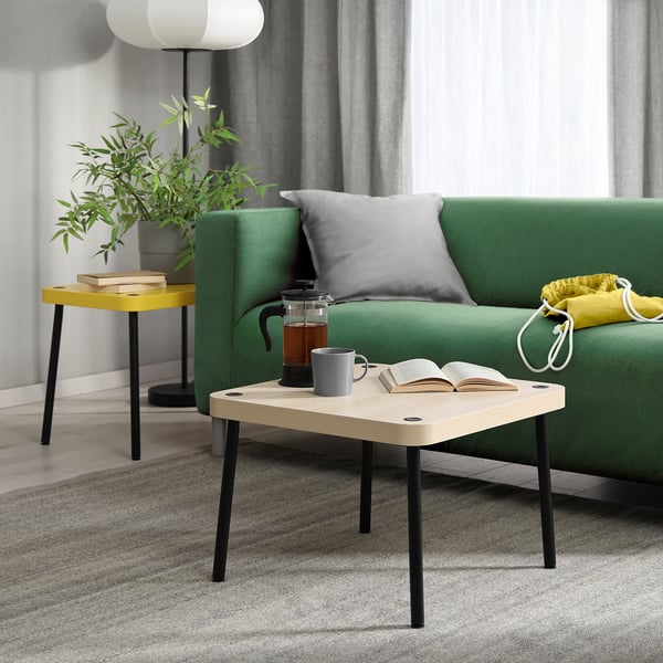 Небольшой приставной столик SONHULT в белом и черном цветах, современный минималистичный дизайн, с кофеваркой, кружкой и книгой рядом с зеленым диваном.