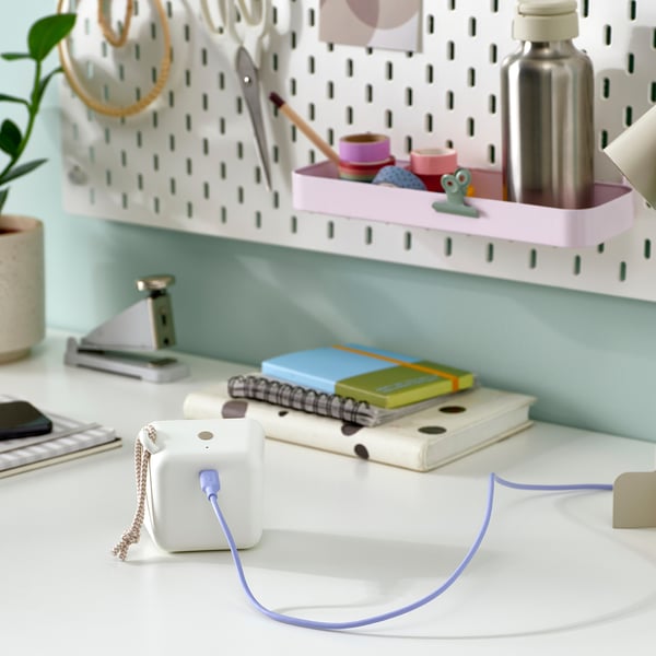 Аккуратно организованный письменный стол с портативной bluetooth-колонкой, красочными блокнотами и канцелярскими принадлежностями на доске.