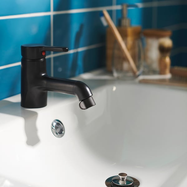 Black modern bathroom tap with white sink and blue tiled wall.