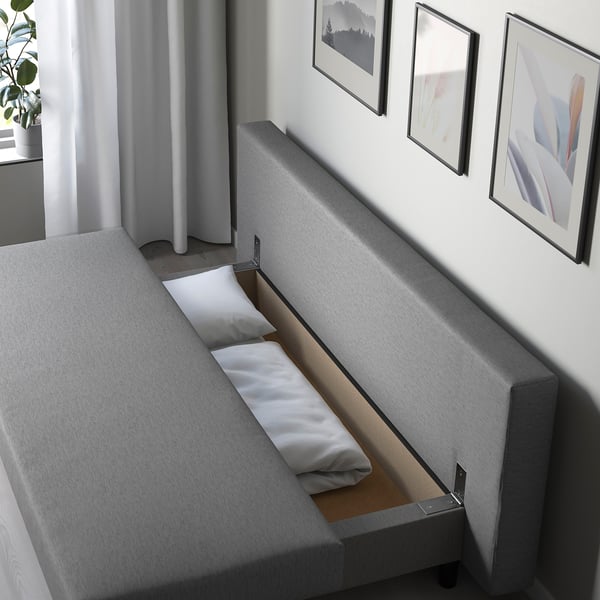 Modern grey sofa with hidden bed mechanism, showing storage underneath and folded mattress section.