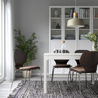 Modern dining setup with ÄLVGRÄSMAL chair pads in beige, positioned on dark brown chairs around a white table on a patterned rug under a hanging lamp.