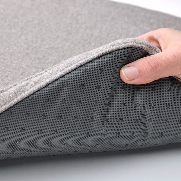 A hand lifts a grey cushion, showcasing textured underside with anti-slip dots for stability.