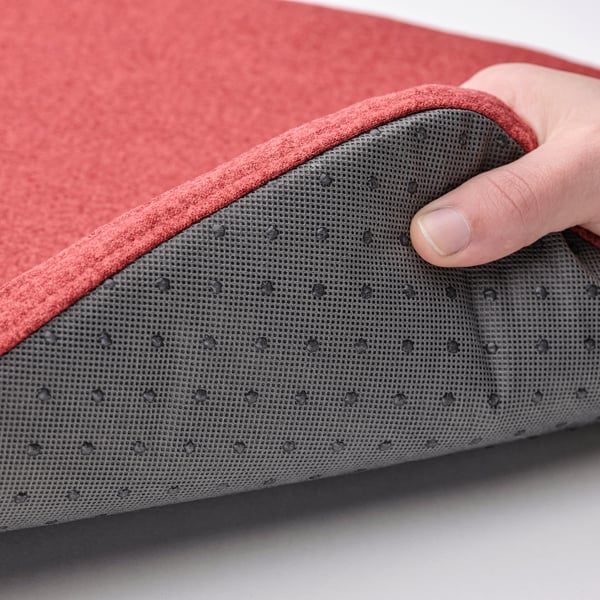 Person holding edge of red ÄLVGRÄSMAL chair pad, showing anti-slip dots.