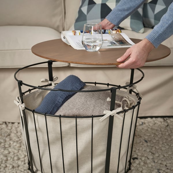 Person holding wooden tray over multi-functional storage table with blankets.