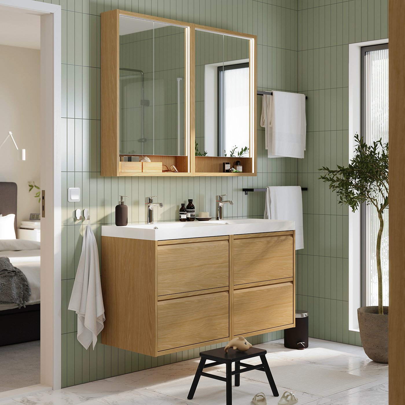 Modern bathroom with ÄNGSJÖN oak vanity, two sinks, mirrors, white towels, green tiles, and stool.