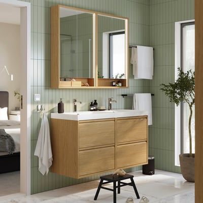 Modern bathroom with ÄNGSJÖN oak vanity, two sinks, mirrors, white towels, green tiles, and stool.