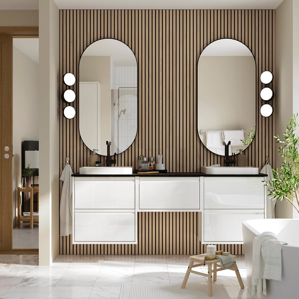 Modern bathroom with white vanity, black mirrors, marble dual sinks, striped wall, stool, plant.