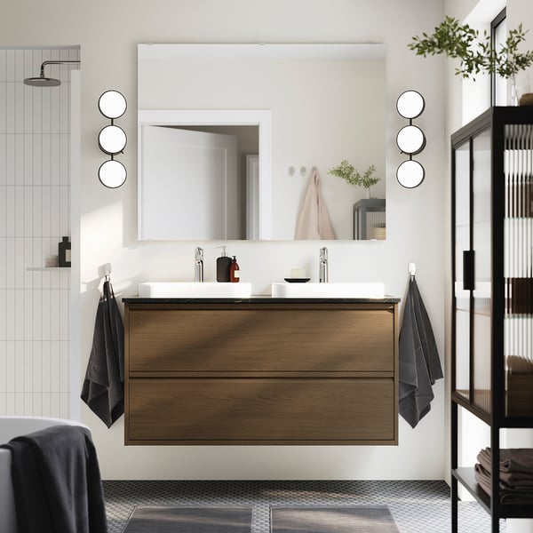 Modern bathroom with dark brown ÄNGSJÖN cabinet, marble sink, large mirror, and black towels.