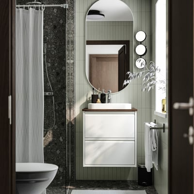 Modern bathroom with ÄNGSJÖN cabinet, wall-mounted sink, mirror, toilet, towel rack, green tiles, and glass shower.
