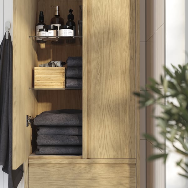 Wooden cabinet with folded towels, bottles, and neatly organised shelves, ideal for bathroom storage.