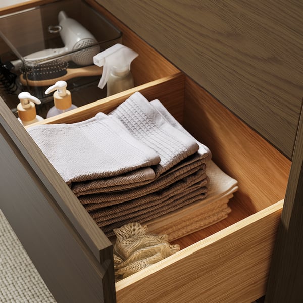 Wooden bathroom drawer with neatly stacked towels and bottles.