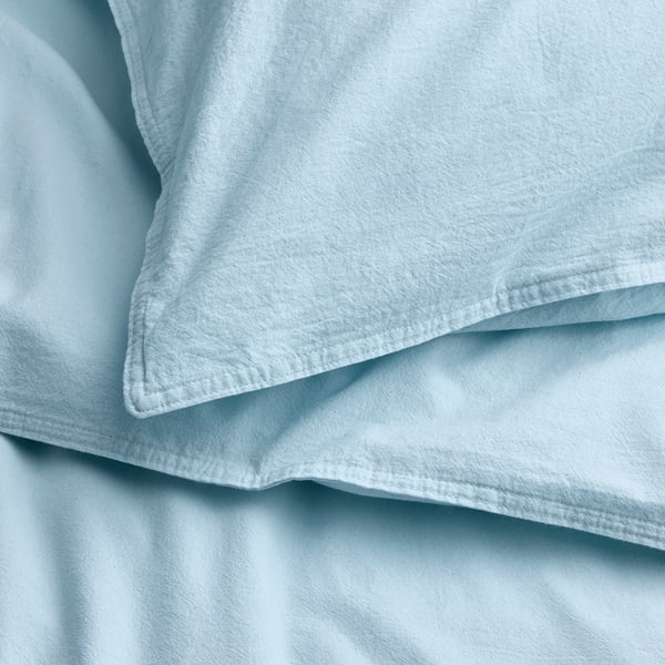 Soft, light blue cotton duvet and pillowcase set, neatly folded, displaying fine stitching and smooth texture.