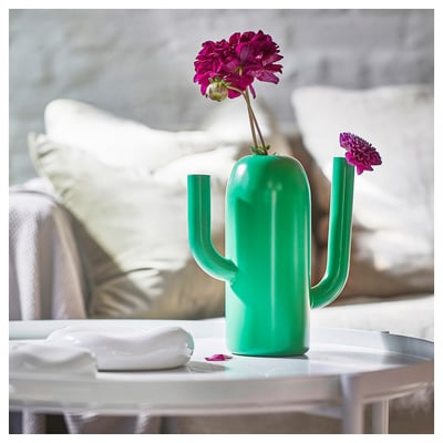 Bright green cactus-shaped watering can vase with pink flowers on table, modern design.