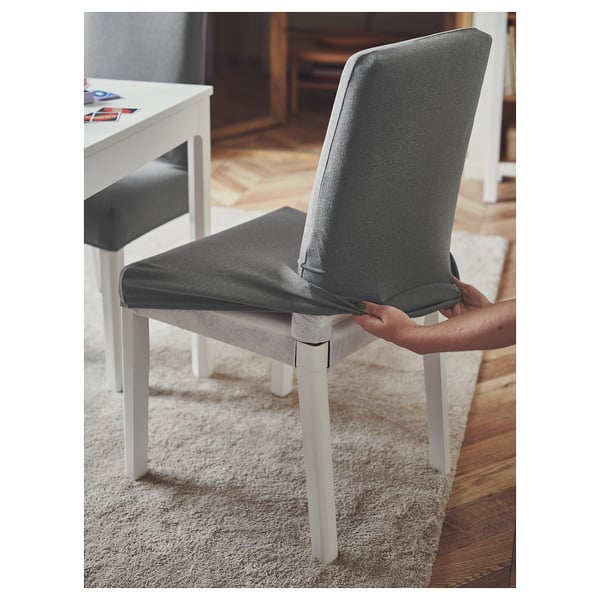 A person places a grey polyester ÄSPHULT chair cover on a white chair.
