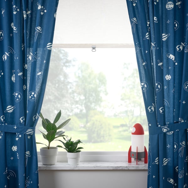 Blue curtains frame a window with plants and a rocket lamp, showing green outdoor views.