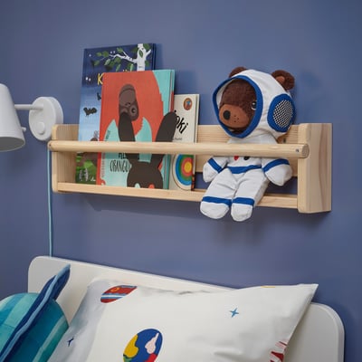 Teddy bear in astronaut suit sits on shelf over bed.