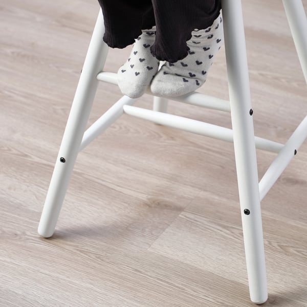 Childs feet in mickey mouse socks rest on footrest of white junior chair, ideal for dining table height.