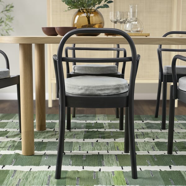 Dining table with black chairs, cushions, green rug, and table decor.