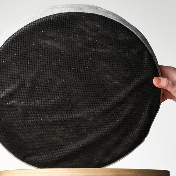 A hand holding a large, round, black memory foam chair pad with a non-slip surface.