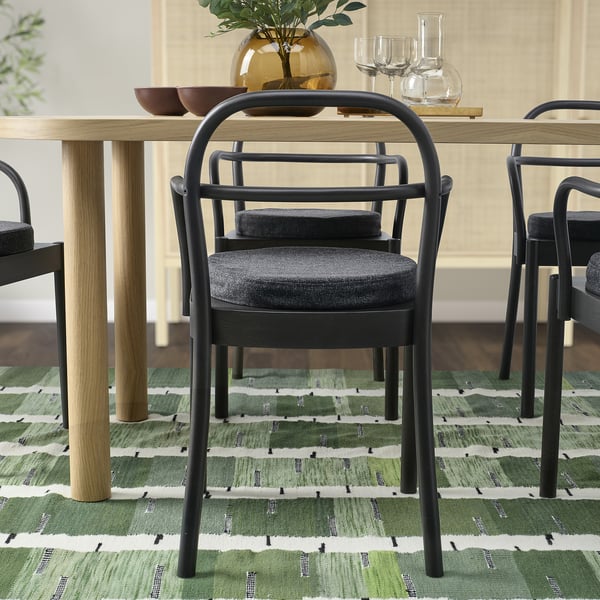 Modern dining set with black metal chairs and wooden table. Chairs have grey cushions, and table holds decorative items.