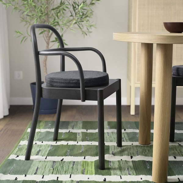 Modern black chair with grey cushion on green striped rug beside wooden table.