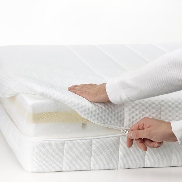 A person is unzipping a white foam mattress, highlighting its removable, washable cover for easy cleaning.