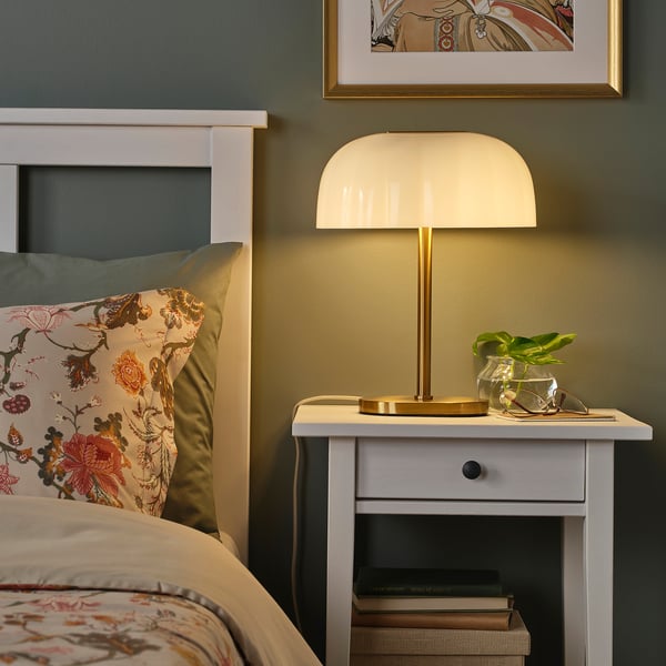 AKTERSPRING table lamp with brass base and glass shade on bedside table, offering warm light in a cozy bedroom.