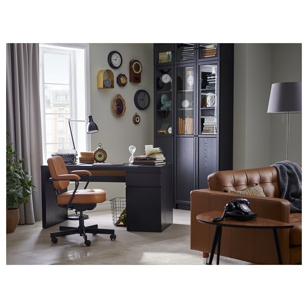 Modern home office with a brown leather office chair, wooden desk, and bookshelves, featuring various clocks and ergonomic setup.
